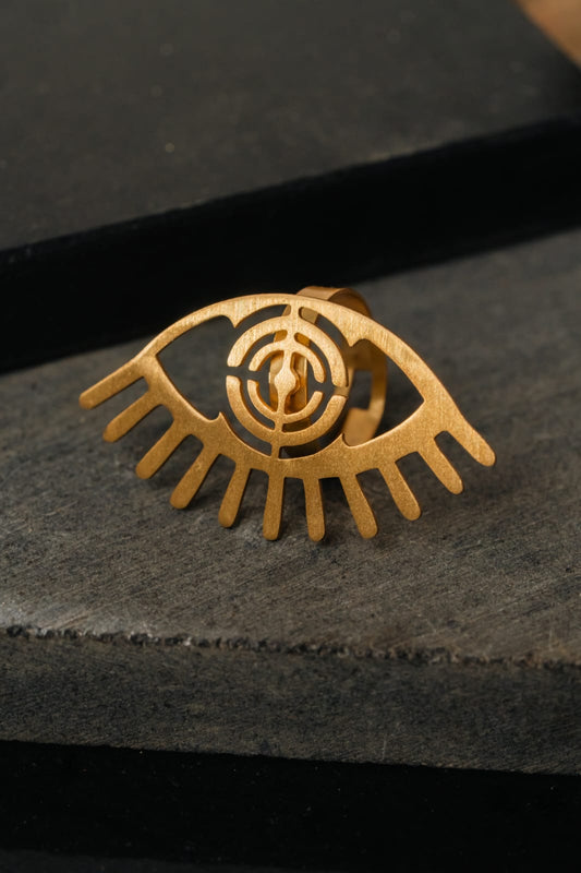 Gold eye-shaped ring on a dark stone surface