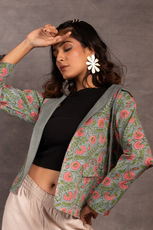 Woman wearing a floral jacket, black top, and beige pants against a gray background